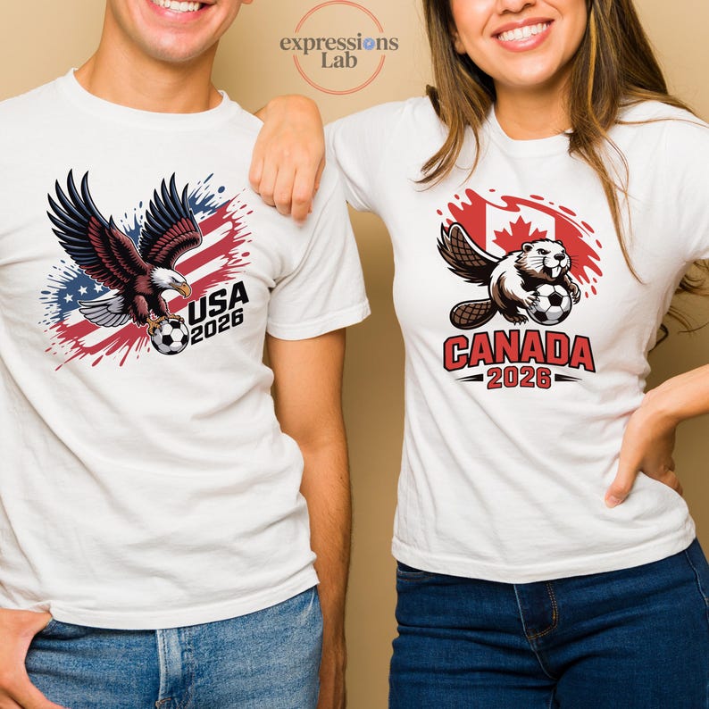 K&ouml;nnte beinhalten: Wei&szlig;e T-Shirts mit grafischen Designs. Eines zeigt einen Adler mit einem Fu&szlig;ball und dem Text "USA 2026". Das andere zeigt einen Biber mit einem Fu&szlig;ball und dem Text "CANADA 2026" vor rotem und wei&szlig;em Hintergrund.