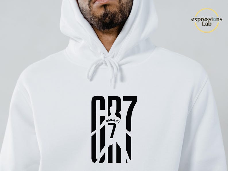 May include: A white hooded sweatshirt featuring a black graphic print on the chest. The design displays the text CR7 with a silhouette of a soccer player wearing a jersey with the number 7 and the name Ronaldo. The logo Expressions Lab is visible.