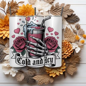May include: White tumbler with a graphic of a skeleton hand holding a drink, surrounded by pink hearts and roses. The text "Cold and Icy" is on a banner. The tumbler has a black straw.