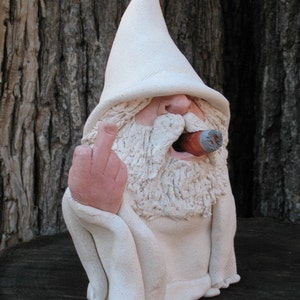 May include: A ceramic garden gnome sculpture with a white pointed hat, beard, and robe. The gnome is holding up its middle finger and has a cigar in its mouth. The sculpture is off-white with pink accents.