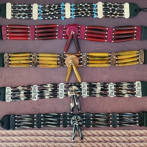 May include: A selection of handcrafted chokers with detailed beadwork and leather detailing. The chokers display a range of colours, including black, red, yellow, and cream, with decorative elements such as turquoise beads and metal accents. Each choker has a unique design.
