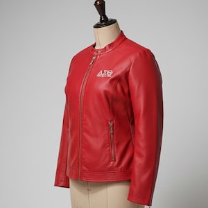 May include: A red leather jacket with a stand-up collar and a front zip. The jacket features a small embroidered emblem on the chest. The jacket is displayed on a mannequin.