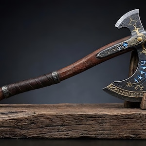 May include: An intricately designed axe with a wooden handle and a metal head. The head features gold and blue detailing, with a dark grey blade. The handle is wrapped in brown leather. The axe rests on a wooden block.