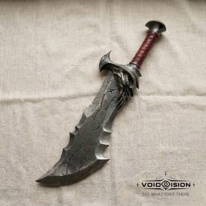 May include: A detailed, fantasy-style blade with a textured, gray blade and a red and brown wrapped handle. The blade has a jagged edge and a decorative hilt. The Void Vision logo and text "SEE WHAT ISN'T THERE" are visible.