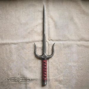 Könnte beinhalten: Eine silberne Sai-Waffe mit einem rot umwickelten Griff. Die Sai hat eine zentrale Klinge und zwei gebogene Zinken. Der Text "+ VOIDOVISION" und "SEE WHAT ISN'T THERE" befindet sich unten.
