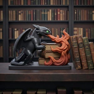 Könnte beinhalten: Schwarze Drachenfigur mit grünen Augen und großen Flügeln, die orangefarbene Flammen ausstößt. Der Drache ist vor einem Stapel Bücher positioniert. Die Figur steht auf einem dunklen Sockel, mit Bücherregalen im Hintergrund.