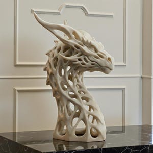 May include: A cream-colored dragon head sculpture with an open, lattice-like design. The sculpture features a detailed face, horns, and a long neck. The artwork is displayed on a black marble surface.