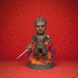 May include: A figurine of a character with dark skin, wearing a brown and gold outfit, holding a sword. The figure has a red eye and stands on a base with flames and a dragon. The background is a solid red.