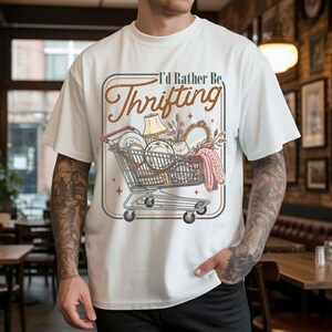 PNG digital design featuring a vintage-style illustration of a shopping cart filled with thrifted items and the phrase “I’d Rather Be Thrifting” in retro typography, isolated on transparent background.