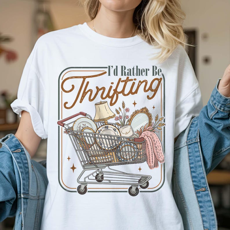 PNG digital design featuring a vintage-style illustration of a shopping cart filled with thrifted home decor items and the phrase “I’d Rather Be Thrifting,” displayed on a white t-shirt mockup.