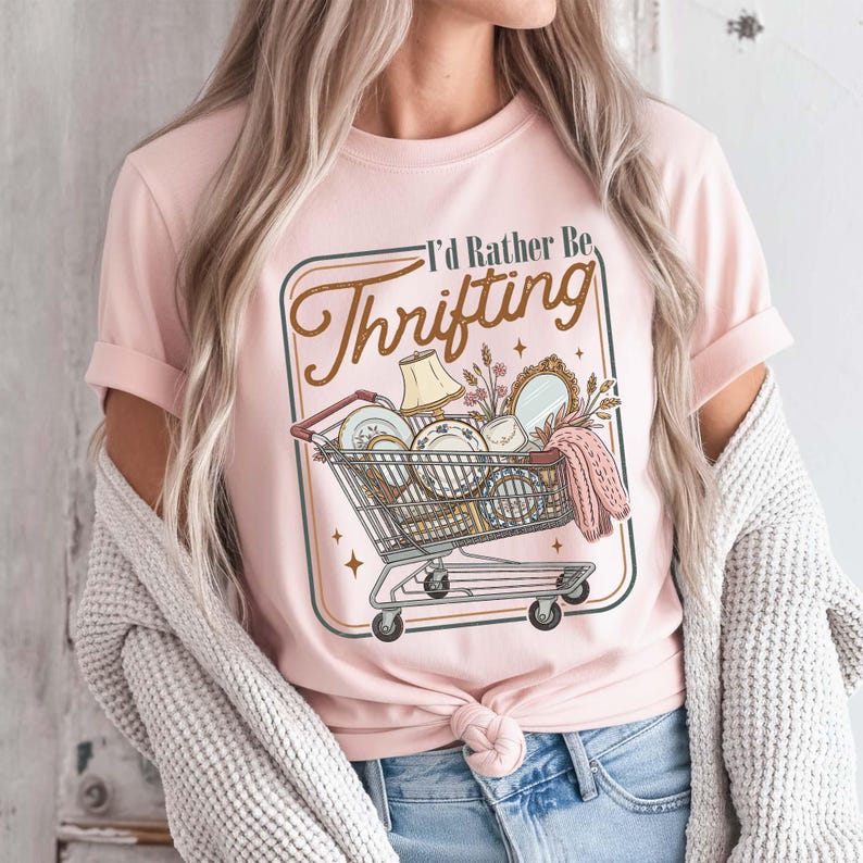 PNG digital design featuring a vintage-style illustration of a shopping cart filled with thrifted home decor items and the phrase “I’d Rather Be Thrifting,” displayed on a pink t-shirt mockup.