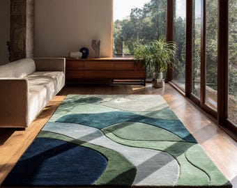 May include: A rectangular area rug featuring an abstract pattern of organic, flowing shapes in various shades of green, deep navy blue, and light gray. The rug has a textured, tufted surface with distinct color-blocked sections and curved lines.