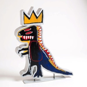 May include: A grey dinosaur sculpture with a yellow and black crown. The dinosaur is painted in black, red, and blue, with a white outline. The sculpture is mounted on a grey base.