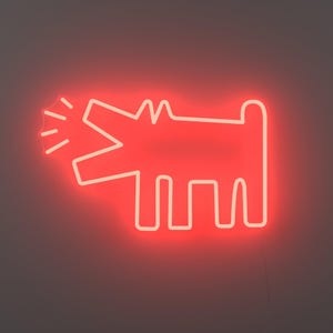 May include: A red neon sign depicting a barking dog. The dog is a simple outline with an open mouth and radiating lines. The sign is mounted on a dark grey wall. The neon light gives off a bright glow.