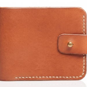 May include: A brown leather wallet with a snap closure. The wallet is rectangular with rounded corners and white stitching along the edges. The snap is a gold-colored metal. The leather has a natural, textured appearance.