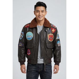 May include: A dark brown leather bomber jacket featuring a brown faux fur collar, ribbed cuffs, and a front zipper closure. The jacket is adorned with numerous colorful embroidered military-style patches on the chest, shoulders, and sleeves.