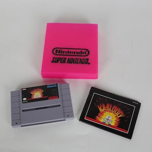 May include: A pink Nintendo Super Nintendo game case, a grey game cartridge, and a game box insert. The cartridge and insert feature the game "Kablooey". The case has the Nintendo logo.