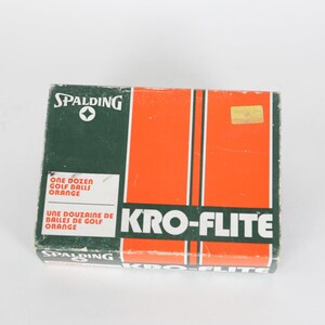 May include: A vintage box of Spalding Kro-Flite golf balls. The box is green and orange with white text that reads "ONE DOZEN GOLF BALLS ORANGE" and "KRO-FLITE". The Spalding logo is visible.