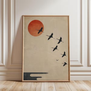 Puede incluir: Impresión artística enmarcada con un diseño minimalista. Un sol rojo está en la esquina superior izquierda, con pájaros negros volando sobre un fondo beige. Una forma oscura en forma de nube está en la parte inferior.