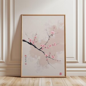 Puede incluir: Impresión enmarcada que presenta una rama de flores de cerezo rosas sobre un fondo suave y neutro. La obra de arte tiene una estética minimalista, con caracteres japoneses y un sello rojo.