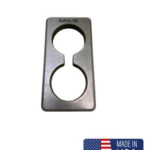 Op de afbeelding: Een zilverkleurige metalen bekerhouder met twee cirkelvormige openingen verbonden door een smal kanaal. De tekst "MX-5" staat bovenaan. Gemaakt in de VS.