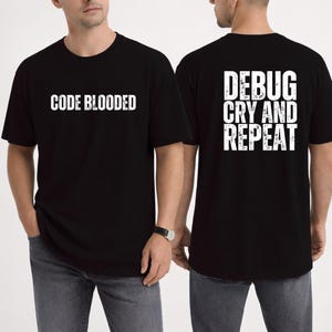 May include: Black t-shirts with white text. One shirt says "CODE BLOODED" on the front. The other says "DEBUG CRY AND REPEAT" on the back. The shirts are worn by a person in grey jeans.