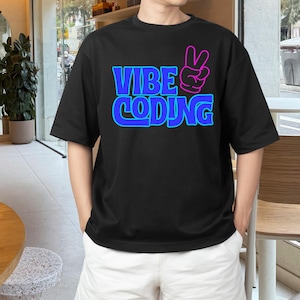 Pode incluir: T-shirt preto com a frase "VIBE CODING" em azul com contorno azul néon. Um sinal de paz rosa e azul acompanha o texto. A t-shirt tem mangas curtas.
