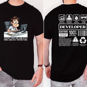 May include: Black t-shirt with a cartoon graphic of a person coding at a desk, and the text "EVERYDAY I WRITE CODE, SOME DAYS IT WORKS, SOME DAYS I PRETEND IT DOES." The back of the shirt has developer-themed graphics and text.