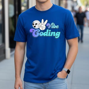 May include: Royal blue t-shirt with the text "Vibe Coding" in a retro font. The graphic includes a peace sign and a smiling face. The shirt is short-sleeved and has a crew neck.