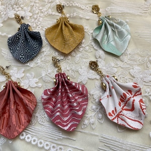 Op de afbeelding: Zes hangende oorbellen met gevouwen stoffen bloemblaadjes in diverse kleuren, waaronder donkerblauw, mosterdgeel, mintgroen, koraal, magenta en wit met rode patronen. Elke oorbel heeft een goudkleurige metalen knop en een kleine ketting.