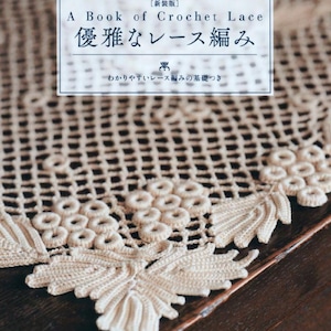 Op de afbeelding: Een boek over Crochet Lace, met Japanse tekst en een crèmekleurig gehaakt kantontwerp. De boekomslag bevat tekst in het Engels en Japans. Het gehaakte kant is gedetailleerd met bloemen- en bladerpatronen.