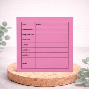 May include: A pink sticky note with black lines and text fields for Age, Name, Session Focus, Long-term Goal, Resources, Activity 1, Activity 2, Activity 3, and Notes. The note is on a cork coaster.