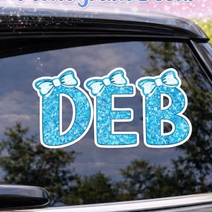 Pode incluir: Um decalque de monograma de laço personalizado com as letras DEB em uma fonte azul brilhante, cada letra encimada por um laço. O decalque é exibido na janela de um carro, com o texto "Custom Bow Monogram Decal" no topo.