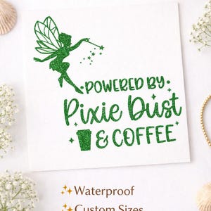 May include: A white vinyl decal with green glitter text and a fairy illustration. The text reads "Powered by Pixie Dust & Coffee Decal" and "Powered by Pixie Dust & Coffee". Additional text indicates the decal is waterproof, available in custom sizes, and is a vinyl decal.