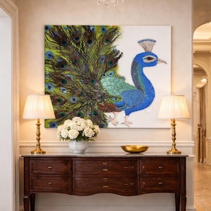 May include: A large painting of a peacock with a vibrant blue body and a detailed tail of green, blue, and brown feathers. The artwork hangs above a dark wood console table with two gold lamps and a white flower arrangement.