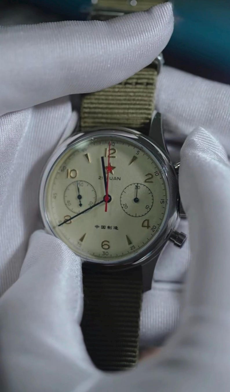 May include: A vintage-style wristwatch with a cream-colored face, black numerals, and a red star at the 12 o'clock position. The watch has two sub-dials and a green canvas strap. The text "Zuan" and Chinese characters are visible on the watch face.