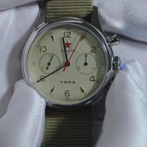 May include: A vintage-style wristwatch with a cream-colored face, black hands, and red second hand. The watch features a stainless steel case and a green nylon strap. The face includes the text "ZIZUAN" and "中国制造".