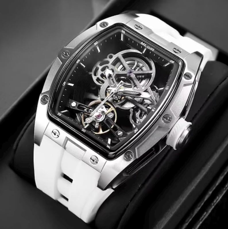 May include: A silver-toned, rectangular watch with a black face and a white silicone band. The watch face has a skeleton design, revealing the inner workings. The watch is displayed on a black surface.