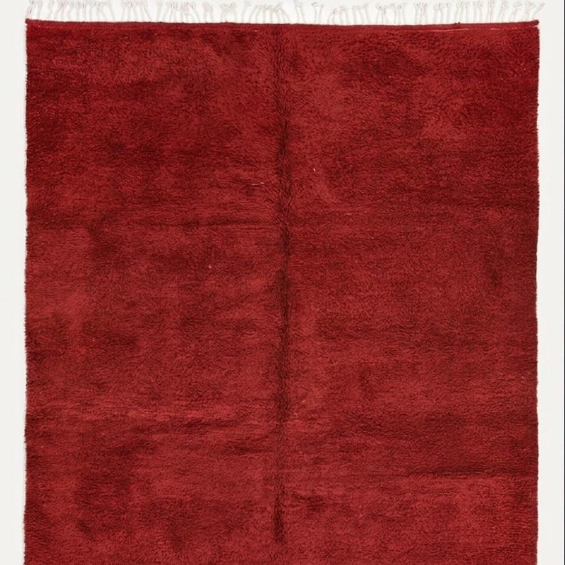 Pu&ograve; includere: Un tappeto rosso rettangolare e morbido con una trama a pelo lungo. Il tappeto &egrave; di colore pieno e ha una frangia di nappe bianche lungo un bordo. Il tappeto &egrave; probabilmente fatto di lana o materiale simile.
