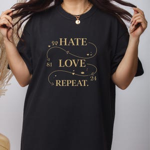 May include: Black t-shirt with gold text that reads "HATE LOVE REPEAT." The text is arranged in a looping design with the numbers 81 and 24. The shirt is a casual, everyday wear item.