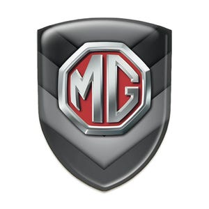 Könnte beinhalten: Ein glänzendes, schildförmiges Emblem mit einem Schwarz-Grau-Verlauf. In der Mitte befindet sich ein rotes Achteck mit den silbernen Buchstaben "MG". Das Emblem hat ein metallisches, dreidimensionales Aussehen.