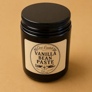 May include: A black jar of Cara's Essentials Vanilla Bean Paste. The label features the text "Vanilla Bean Paste" in a circular design with vanilla bean illustrations. The jar contains 4 oz (113g) of paste.