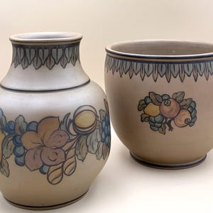 May include: Two ceramic vases with hand-painted fruit and floral designs. The vase on the left is a tall, rounded shape with a narrow neck. The vase on the right is a wide, round planter. Both have a beige background with blue and brown accents.
