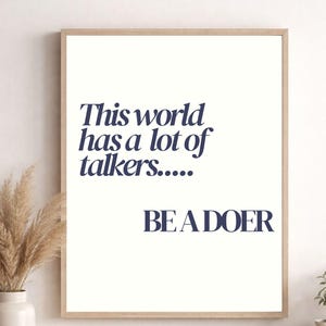Op de afbeelding: Een ingelijste print met de marineblauwe tekst "This world has a lot of talkers..... BE A DOER" op een witte achtergrond. De lijst is lichtbruin.