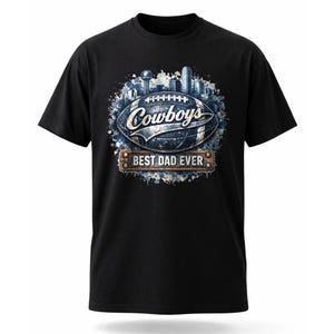 May include: Black t-shirt featuring a football design with the word "Cowboys" and a cityscape graphic. Below the football is a banner that reads "BEST DAD EVER". The design is in shades of blue, white, and brown.