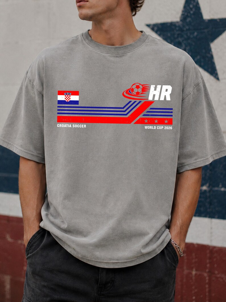 May include: A grey short-sleeve t-shirt featuring a graphic with the Croatian flag, a soccer ball, and the text "HR", "CROATIA SOCCER", and "WORLD CUP 2026". The design includes horizontal blue and red stripes with three small stars.