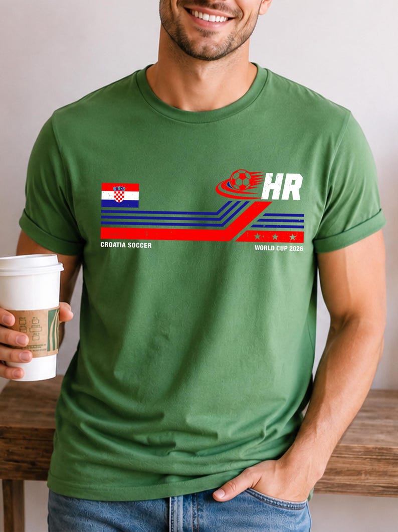 May include: A green short-sleeve t-shirt featuring a graphic with the Croatian flag, a soccer ball, and the text "CROATIA SOCCER" and "HR WORLD CUP 2026". The design includes horizontal blue and red stripes and three small stars.