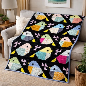 May include: A black quilt with a repeating pattern of colourful, geometric birds. Each bird is made from various patterned fabrics in shades of yellow, blue, pink, and green. The quilt has a light blue border and is draped over a grey sofa.