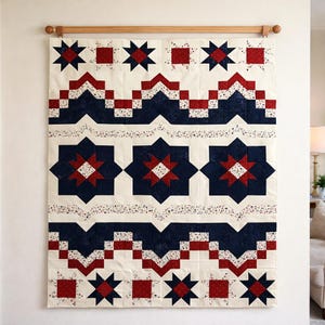 May include: A large, rectangular quilt with a repeating pattern of red, white, and navy blue stars and geometric shapes. The quilt is hung on a wooden rod against a white wall. The design features alternating rows of stars and blocks.