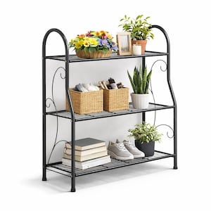 May include: A black metal three-tier shelf unit with decorative scrollwork. The shelves hold plants, books, shoes, and woven baskets. The top shelf has a basket of flowers, a framed photo, and potted plants.